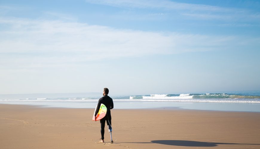 Foto de surfero con pierna protésica en la arena de la playa